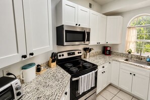 A kitchen with white cabinets, a black stove, a microwave, a coffee maker, and a window with a view of greenery. - Top-Rated ILM Oasis: Spacious, Pet-Friendly, Pool! (Wilmington)