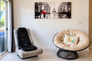 A room with a wheelchair, a cushioned chair, and a painting of the Eiffel Tower. - Top-Rated ILM Oasis: Spacious, Pet-Friendly, Pool! (Wilmington)