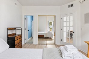Un dormitorio con cama, cómoda de madera, baño con ducha y puerta que da a un balcón.