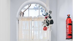 Una cocina con encimera de granito, armarios blancos, un lavamanos de acero inoxidable y un grifo rojo, además de una ventana con cortinas de gasa.