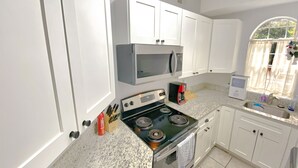 Una cocina con armarios blancos, microondas, estufa y fregadero.