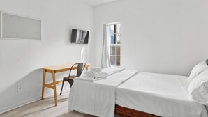 A minimalist bedroom with a single bed, a desk, and a TV. - Bright, Clean, Modern 2BR Luxury Apt UNCW-Beach (Wilmington)