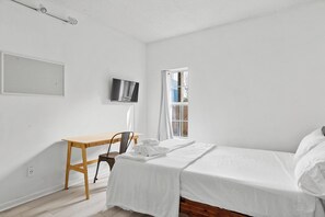 Un dormitorio minimalista con una cama individual, un escritorio y un televisor.