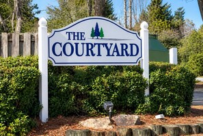 Ein Schild für 'The Courtyard' mit schlichtem Design, weißem Hintergrund und einem Logo mit zwei Bäumen.