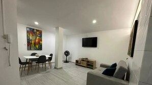 Ein modernes Wohnzimmer mit Essbereich, einem grauen Sofa, einem Flachbildfernseher und einem farbenfrohen abstrakten Gemälde an der Wand.