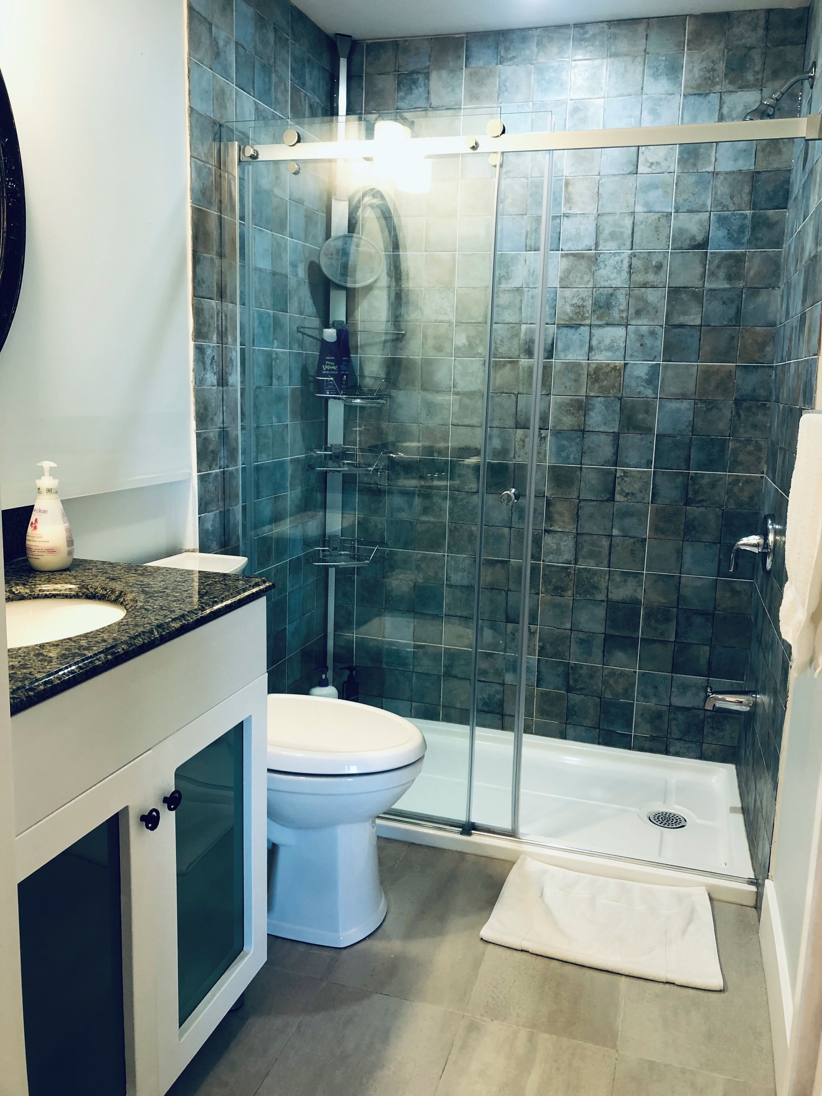 Un baño moderno con ducha envuelta en vidrio, inodoro blanco y encimera de granito con lavamanos.