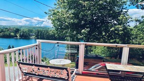 Eine Holzterrasse mit einer Bank und einem Tisch, mit Blick auf einen See und bewaldete Hügel.