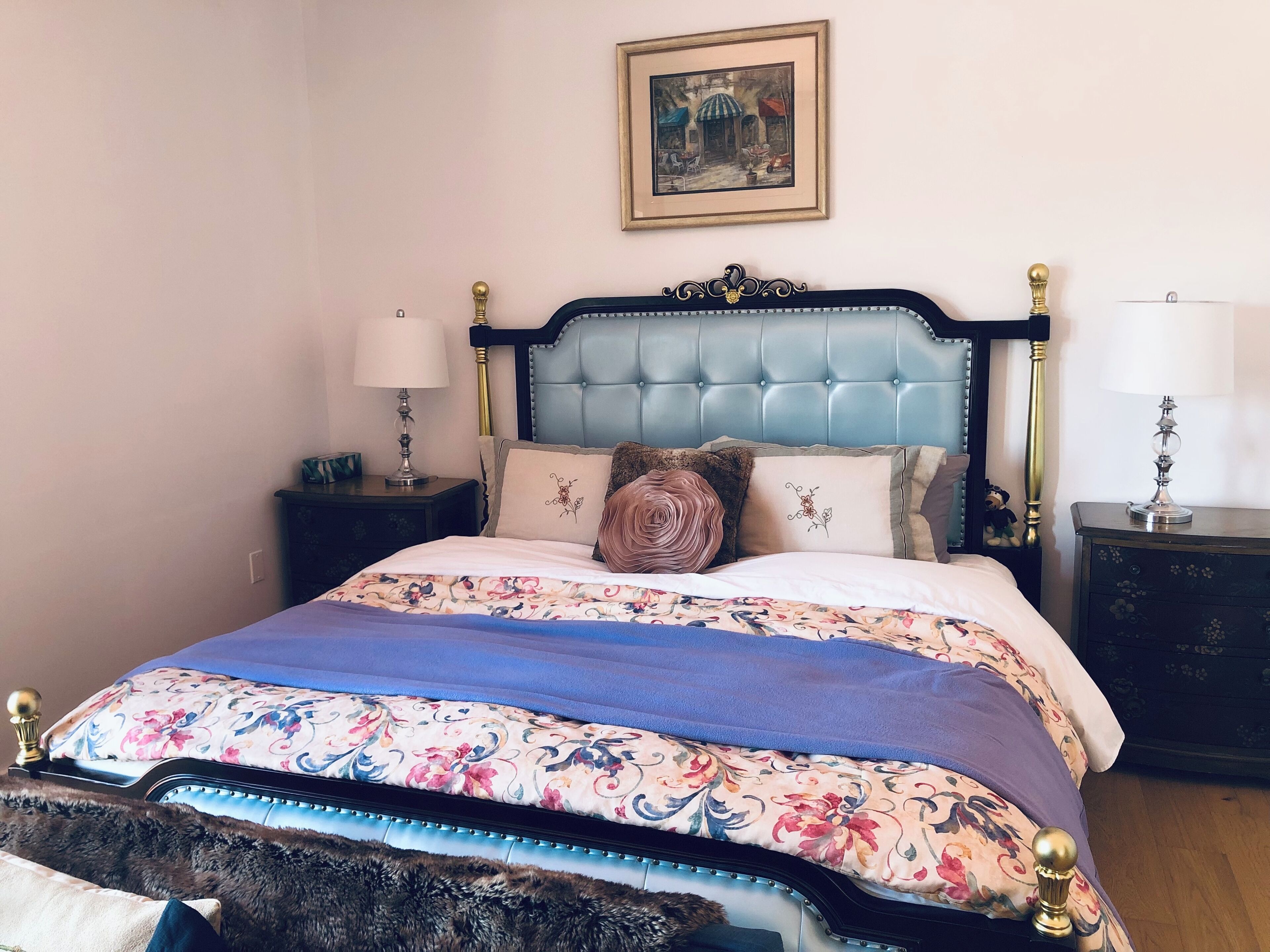 Una cama con cabecera capitonada, ropa de cama floral y almohadas decorativas.