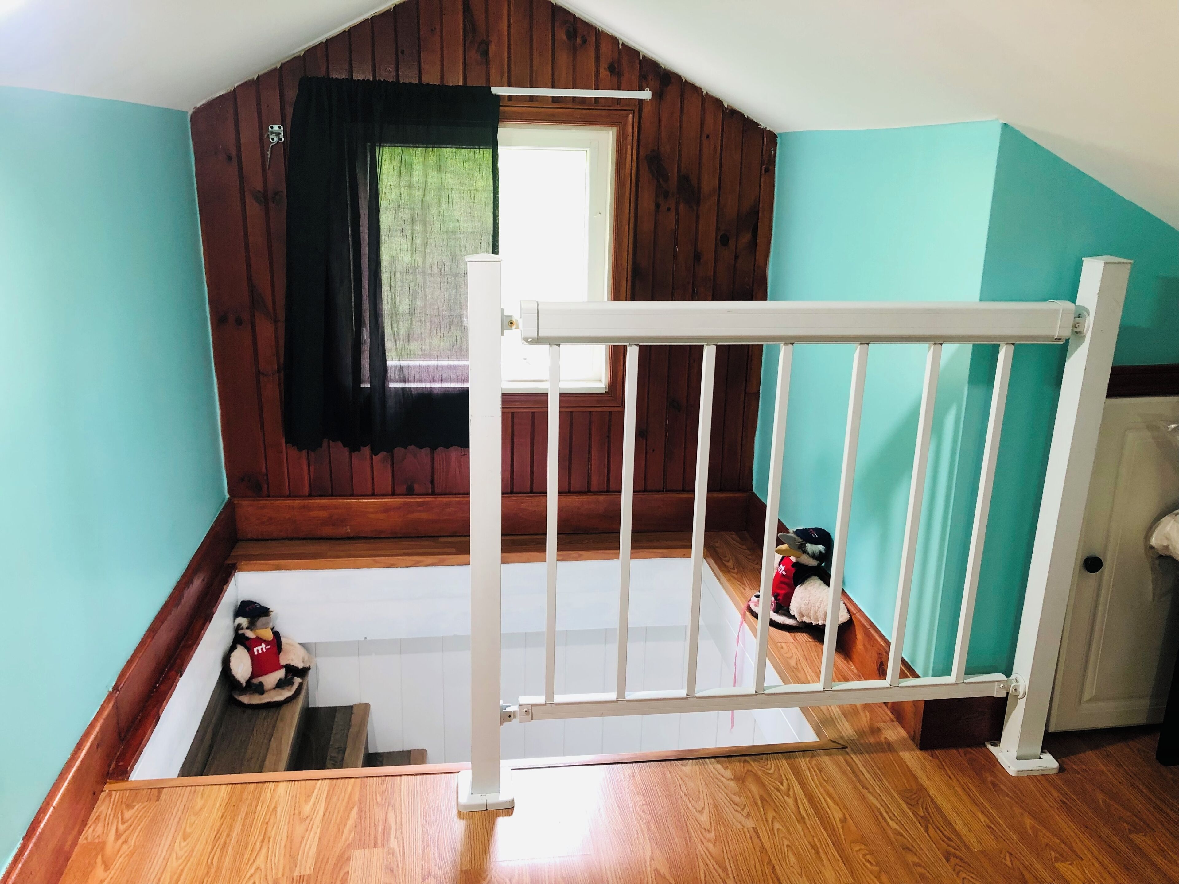 A room with a wooden floor, a white railing, a window with a black curtain, and a door.