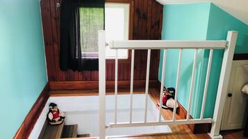 A room with a wooden floor, a white railing, a window with a black curtain, and a door.