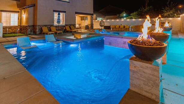 Zona de piscina exterior bien iluminada, con sillones de descanso y una chimenea.