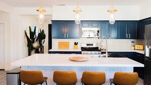 Una cocina moderna con una isla central, armarios azul oscuro y electrodomésticos de acero inoxidable, e iluminada por tres lámparas colgantes.