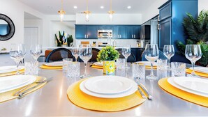 Un comedor moderno con una mesa larga dispuesta para una comida, que incluye copas, platos y cubiertos.