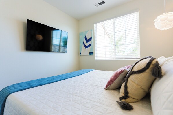 Un dormitorio con cama, una ventana con persianas, una obra de arte colgada en la pared y una rejilla de ventilación en el techo.