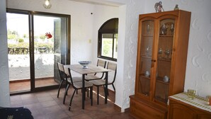 Een eetgedeelte met een tafel en stoelen, een houten kast met glazen deuren, en uitzicht door een schuifdeur naar een buitenbalkon.