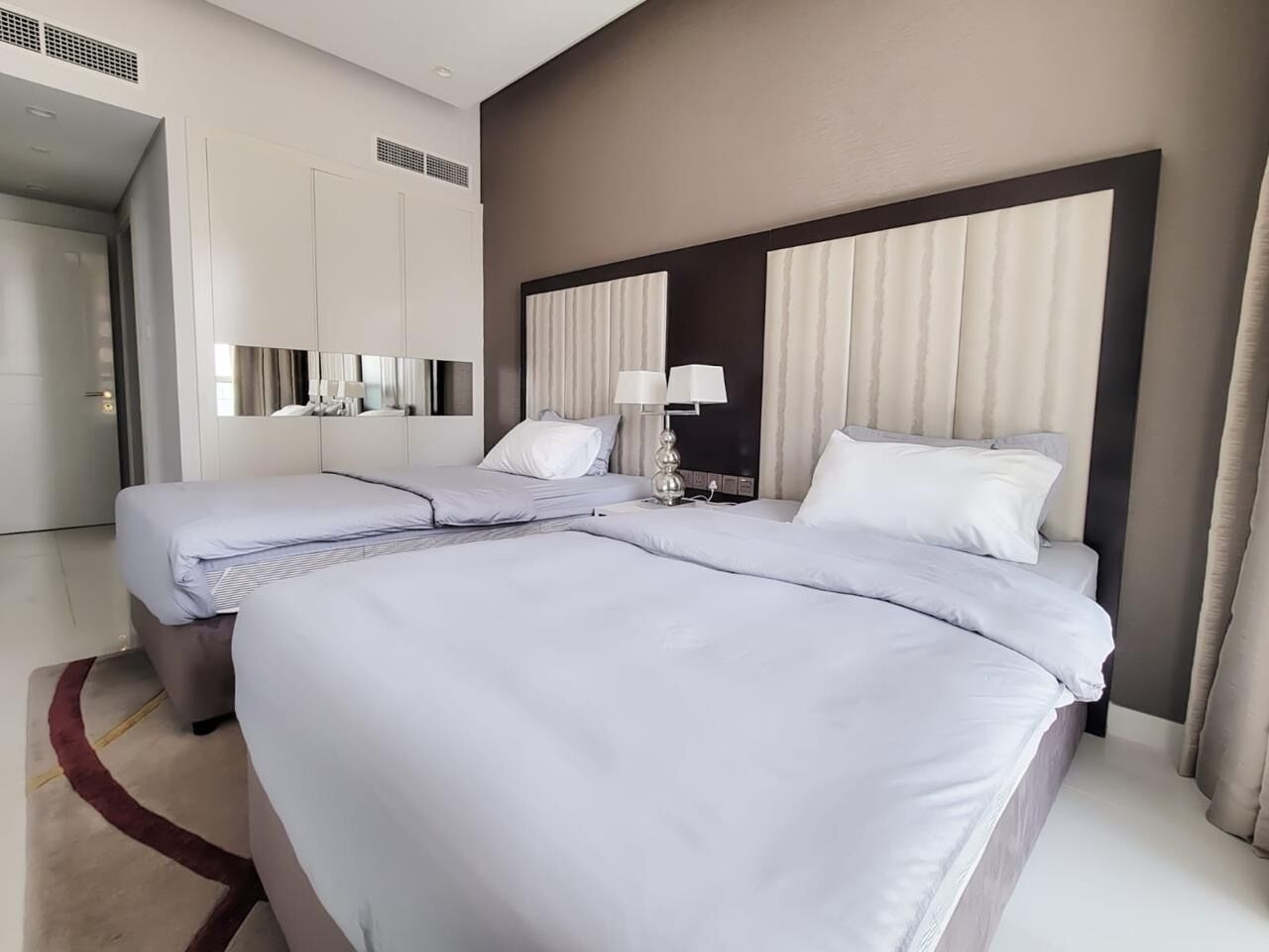 A modern hotel room with a large bed, two bedside tables, a mirror, and a headboard with curtains.