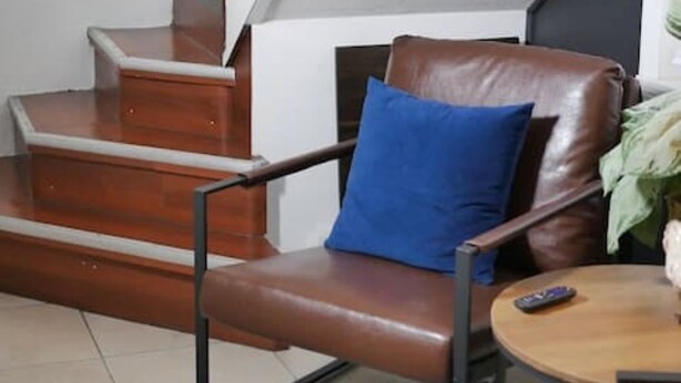 Ein Wohnzimmer mit einem braunen Ledersessel, einem blauen Kissen, einem Holztisch und einer Treppe mit Holzstufen.