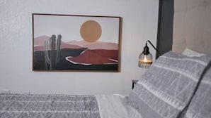 Ein Schlafzimmer mit einem Bett, einer Wandleuchte und einem gerahmten Bild einer Wüstenlandschaft.