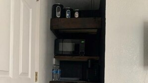 Eine kleine Küche mit einem schwarzen Kühlschrank, einer Mikrowelle und einem Regal mit Küchenutensilien.