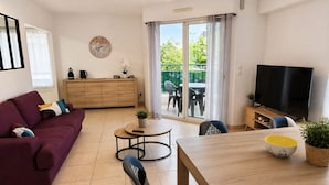 A modern living room with a sofa, a dining table, a TV, and a view through a sliding glass door.