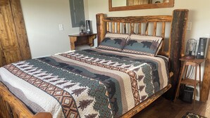 A wooden bed with a patterned quilt, a nightstand with a lamp, and a mirror on the wall. - Tiny house hideaway just outside of town (Cody)