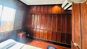 Una habitación con paneles de madera, un ventilador de pie y una ventana con barrotes.