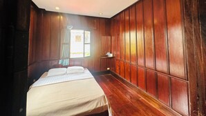 Una habitación con paneles de madera, una cama con ropa blanca, una ventana con cortinas y un pequeño estante con objetos.