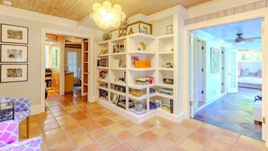 A spacious hallway with a tiled floor, white shelving units filled with books and decorative items, and a ceiling fan. - Sarasota Botanical Garden 3Br Retreat - Near Bay (Sarasota)