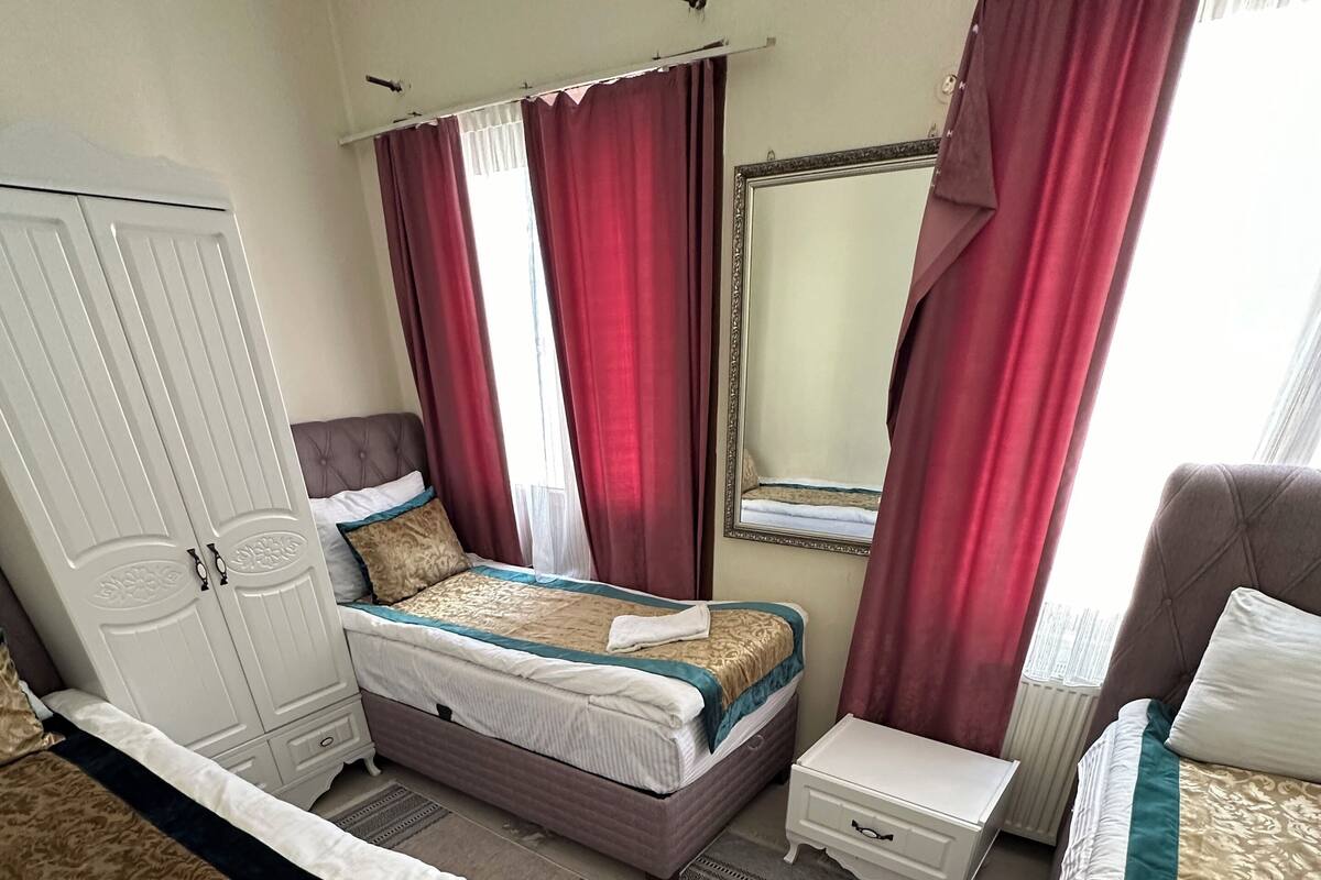 A hotel room with a bed, a small table, a chair, a wardrobe, and a window with curtains.