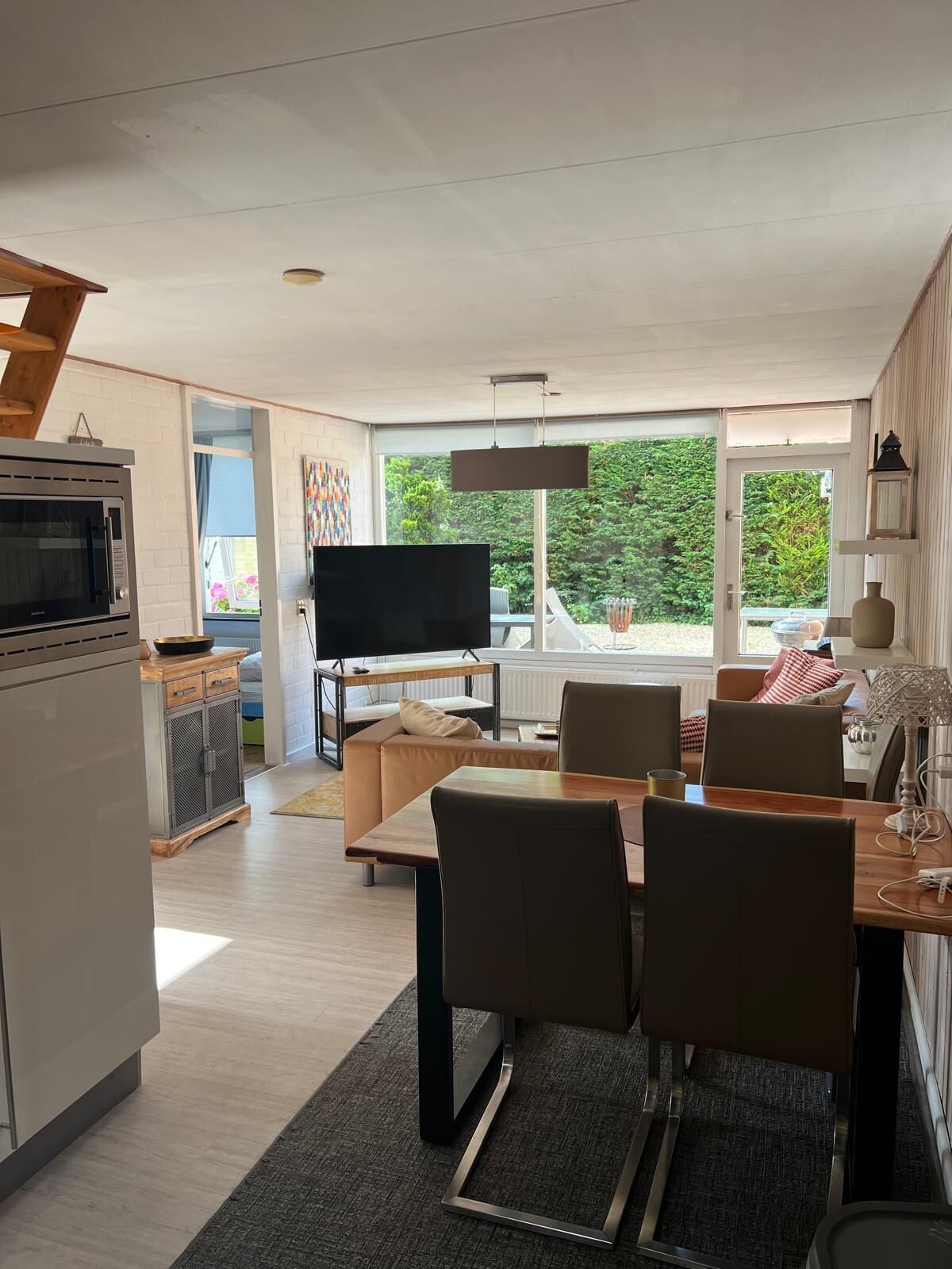 Una cocina moderna con horno y microondas integrados, un comedor con mesa y sillas de madera, y un amplio ventanal con vistas a zonas verdes.