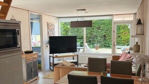 Una cuina moderna amb forn i microones integrats, zona de menjador amb taula i cadires de fusta, i una finestra gran amb vistes a vegetació.