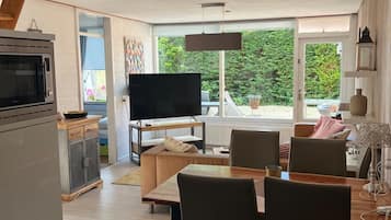 Een moderne keuken met een ingebouwde oven en magnetron, een eethoek met een houten tafel en stoelen, en een groot raam met uitzicht op groen.