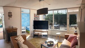 Un saló modern amb una gran televisió de pantalla plana, un sofà, una taula de centre i una zona de menjador amb taula i cadires.