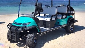 Une voiturette de golf sur une plage de sable, avec l’océan en arrière-plan.