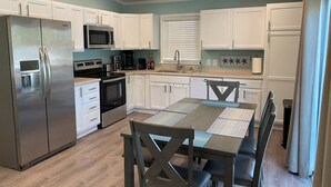 Une cuisine moderne avec des meubles blancs, des appareils en acier inoxydable et un coin repas comprenant une table et des chaises.