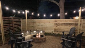 Une terrasse extérieure avec un foyer, deux fauteuils Adirondack et des guirlandes lumineuses.