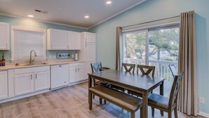 Une cuisine moderne avec des meubles blancs, une table à manger en bois avec des bancs, et une grande fenêtre avec des rideaux.