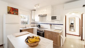 A modern kitchen with white cabinets, a microwave, a stove, and a sink. There is a fruit basket on the counter.