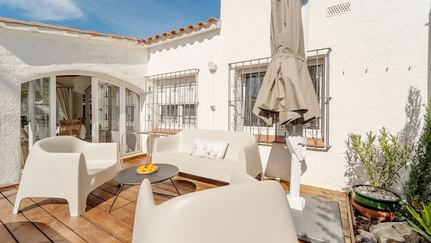 An outdoor patio with white furniture, a table with fruit, and a potted plant.