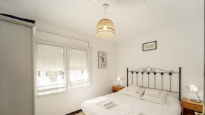 A bedroom with a bed, two bedside tables, a hanging light fixture, and a window with blinds.