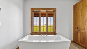 Une salle de bain moderne avec une baignoire sur pieds, une fenêtre en bois donnant sur un champ verdoyant et des meubles en bois.