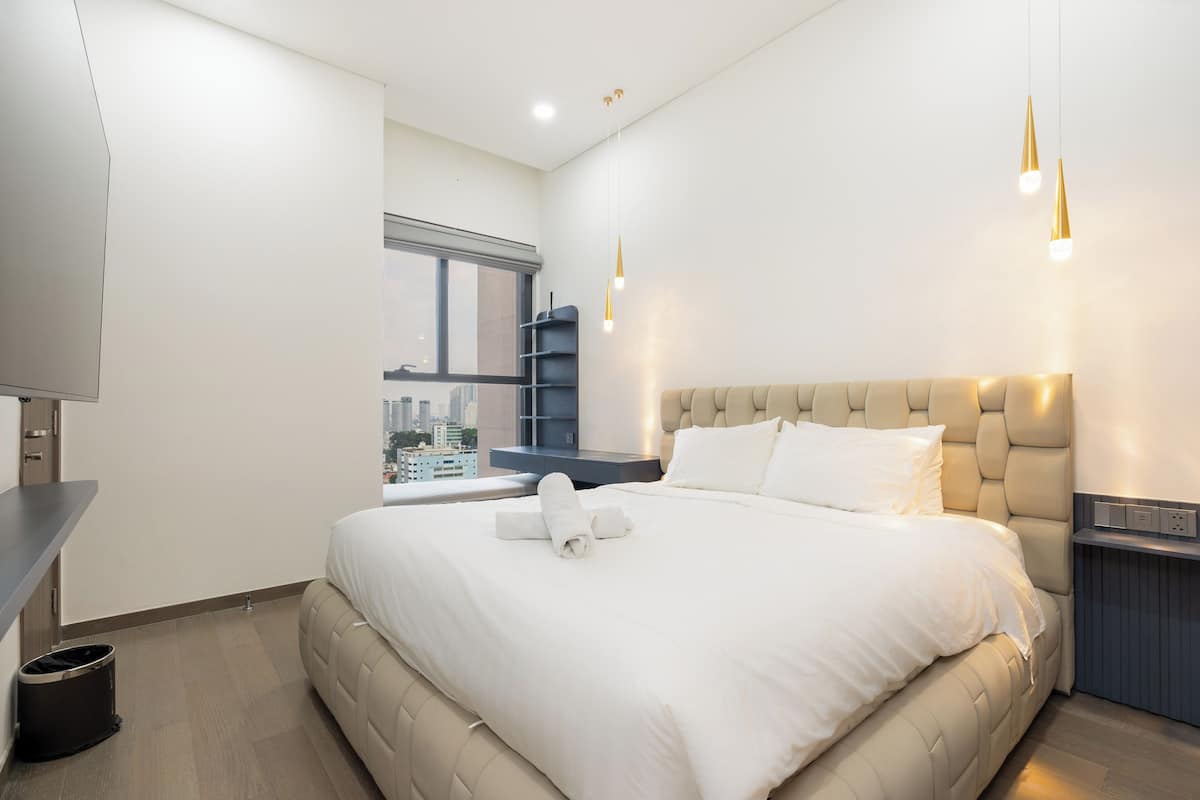 Une chambre d’hôtel moderne dotée d’un grand lit, offrant une vue sur la ville, et présentant un design minimaliste.
