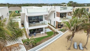 Ein modernes, mehrstöckiges Gebäude mit Dachterrasse, Pool und Strandbereich mit Liegestühlen.