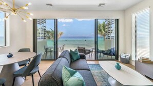 Ein modernes Wohnzimmer mit einer großen Couch, einem Esstisch und Stühlen. Es verfügt über eine große Schiebeglasdoor, die auf einen Balkon mit Meerblick führt.