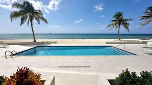 Ein Pool mit Blick auf Strand und Meer, umgeben von Palmen und Liegestühlen.