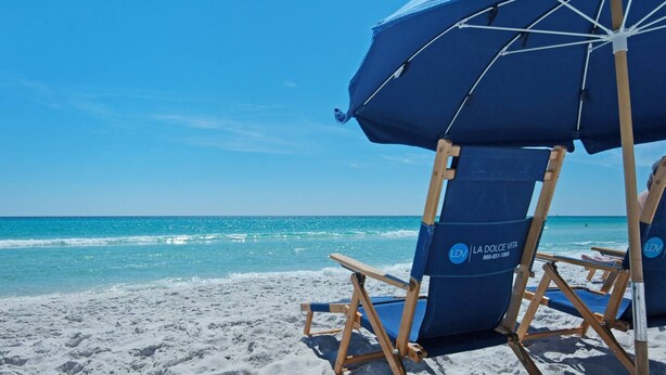 A beach chair with a blue umbrella and a logo on the backrest. - Pet & Family Friendly, Walk or Tram 2 Private Beach Access Pavilion, Pools, Tennis - Emerald Shores (Miramar Beach)