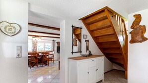 Un escalier avec des rampes en bois, un meuble blanc avec des tiroirs et un coin repas avec des chaises et une table en bois.