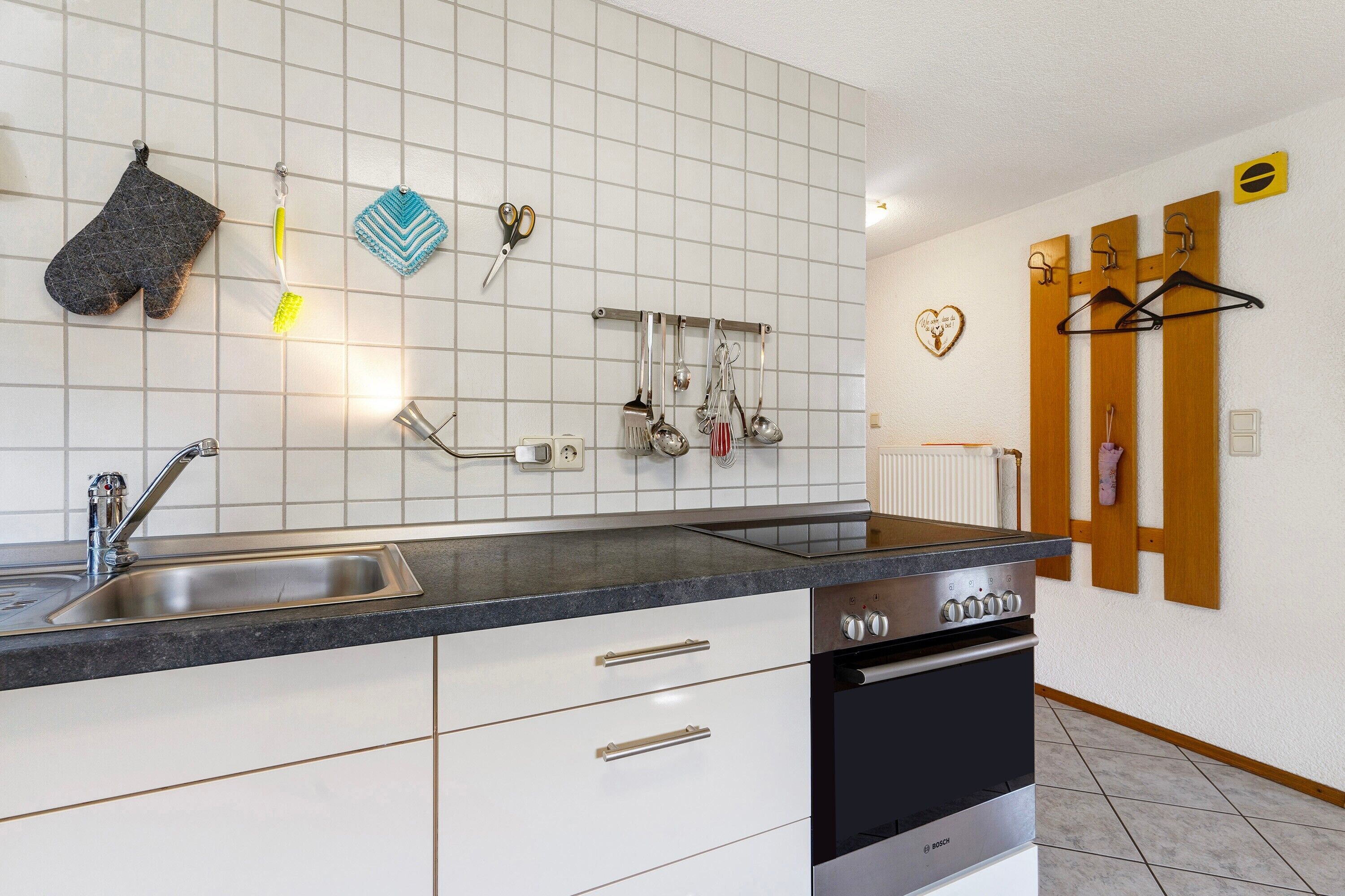 A kitchen with a sink, stove, and hanging utensils.