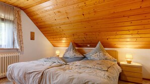 Une chambre avec un plafond en pente, un lit avec une literie à motifs, deux tables de chevet avec des lampes et un radiateur.