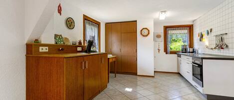 Una cocina con armarios de madera, suelo de baldosas, una ventana con cortinas y un reloj en la pared.